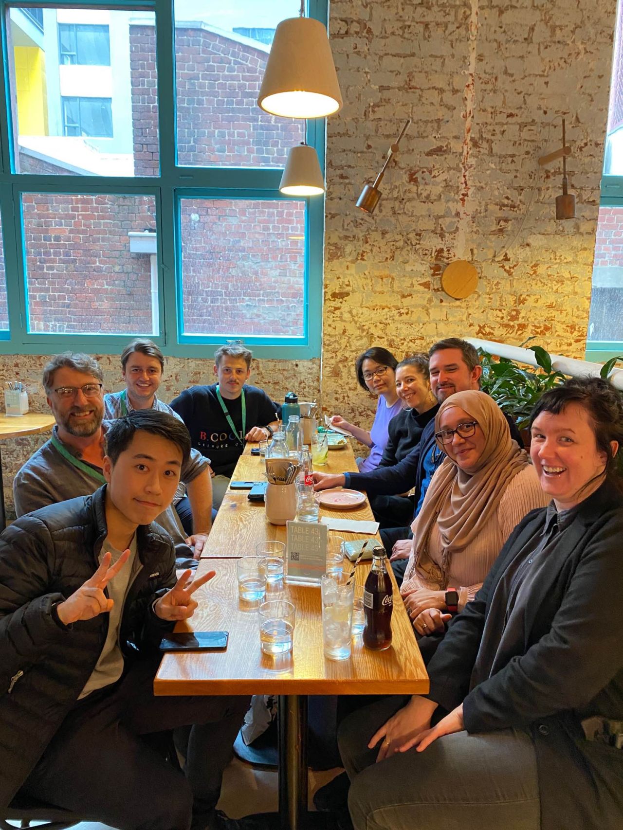 Diverse Avanade Experience Design colleagues smiling together around a long table in a café, exposed brick and large windows