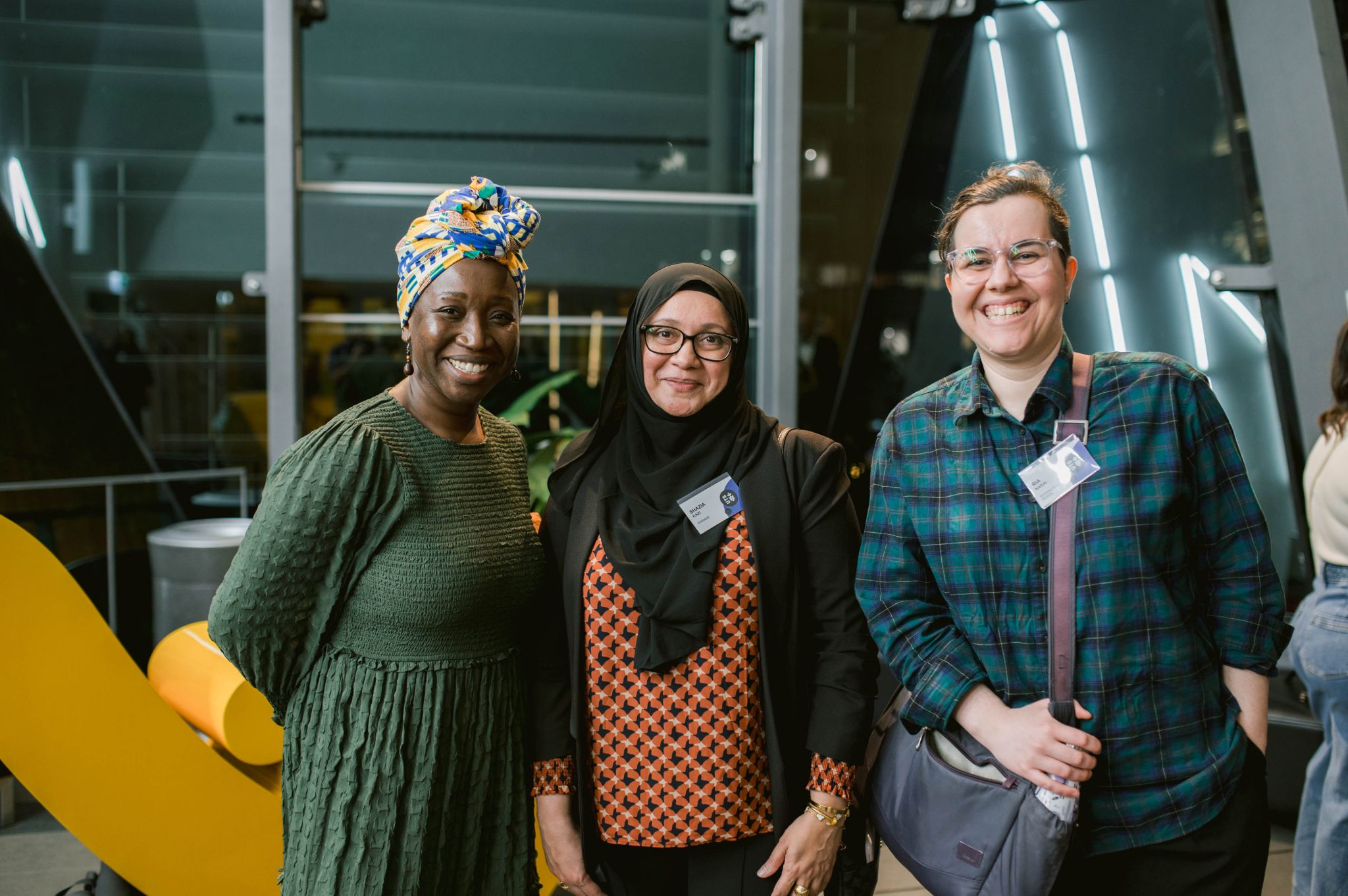 Three women smiling together at a professional conference with name badges.