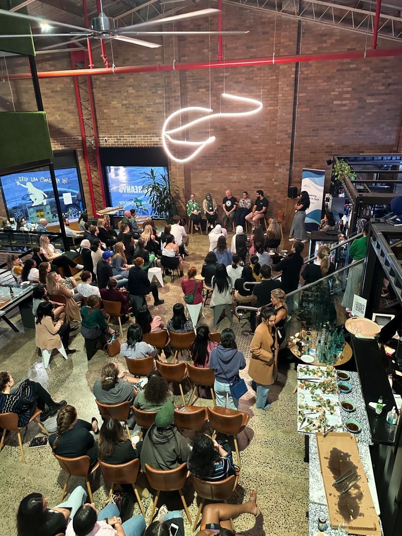 Wide view of Empowering Women in Tech panel with audience seated in an industrial-style venue.