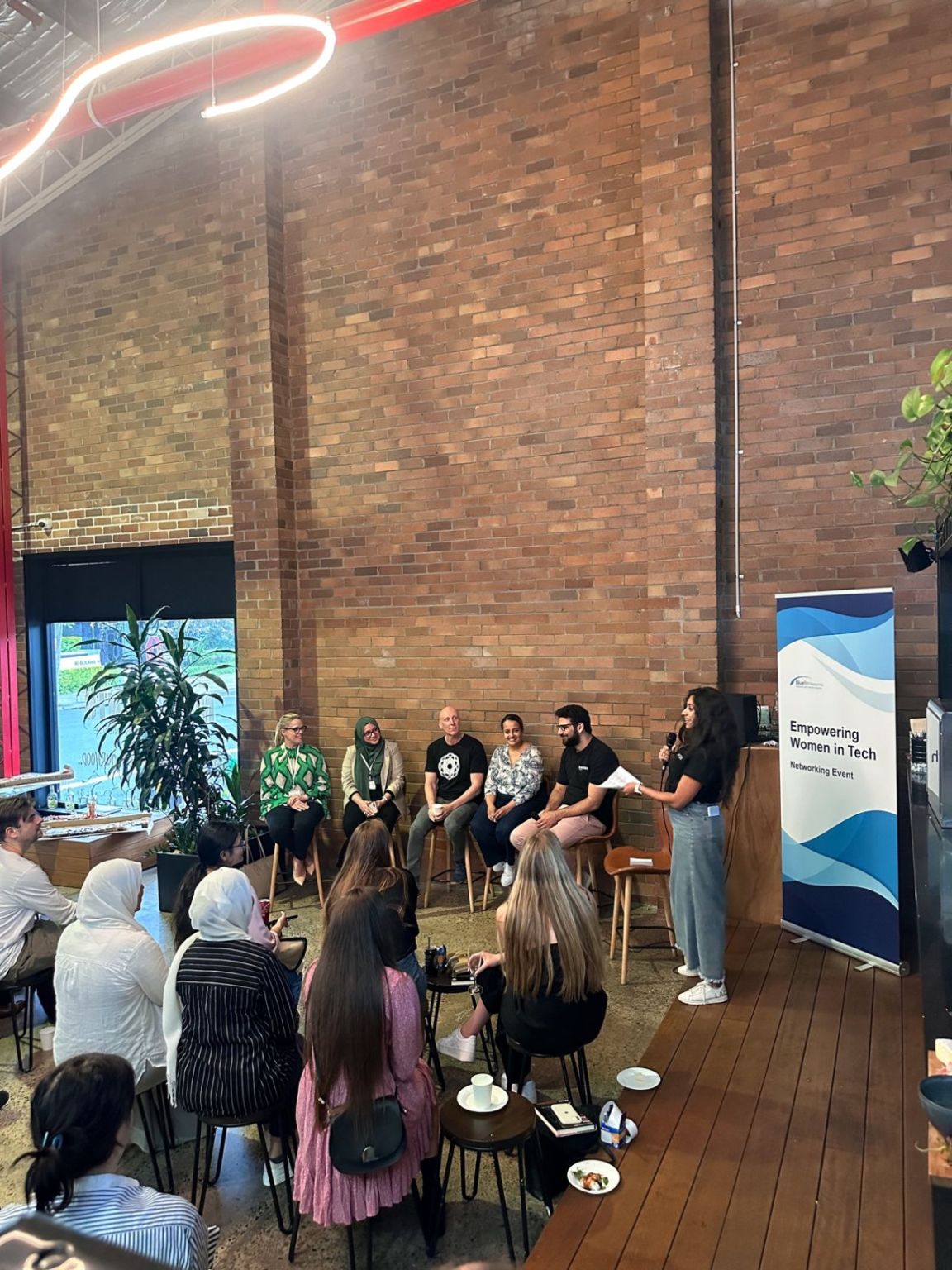 Facilitating an Empowering Women in Tech networking event — on stage with a microphone in front of panelists and audience.
